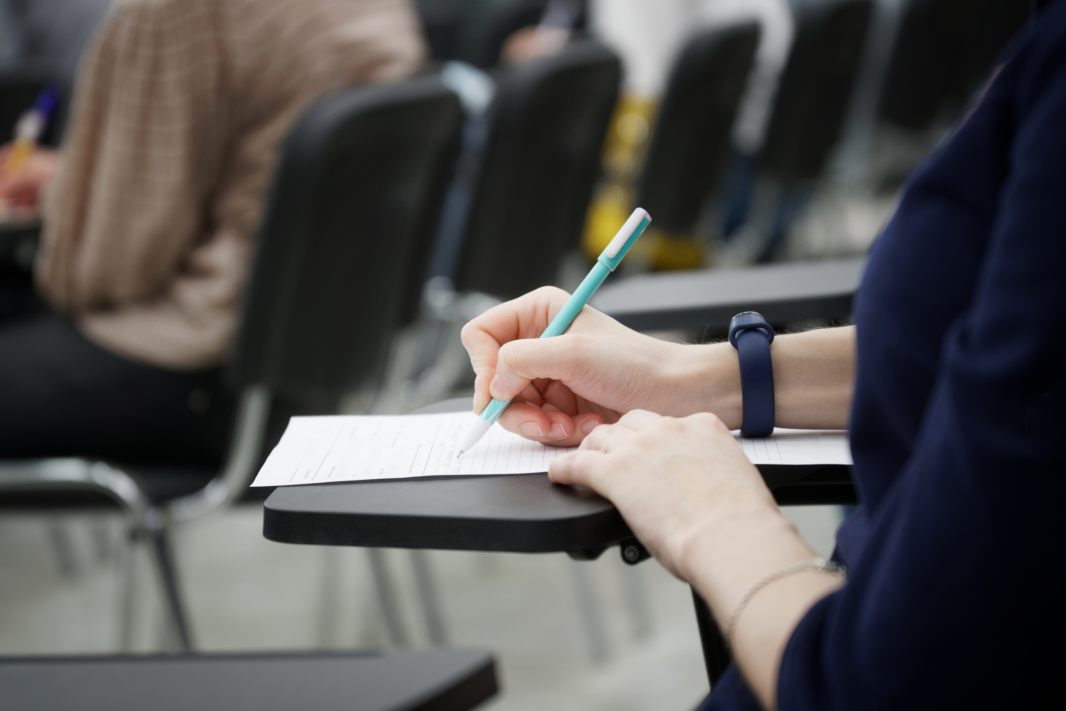 Mano de persona rellenando examen en un aula